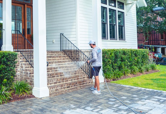 Pressure washing technician spraying brick stairs.